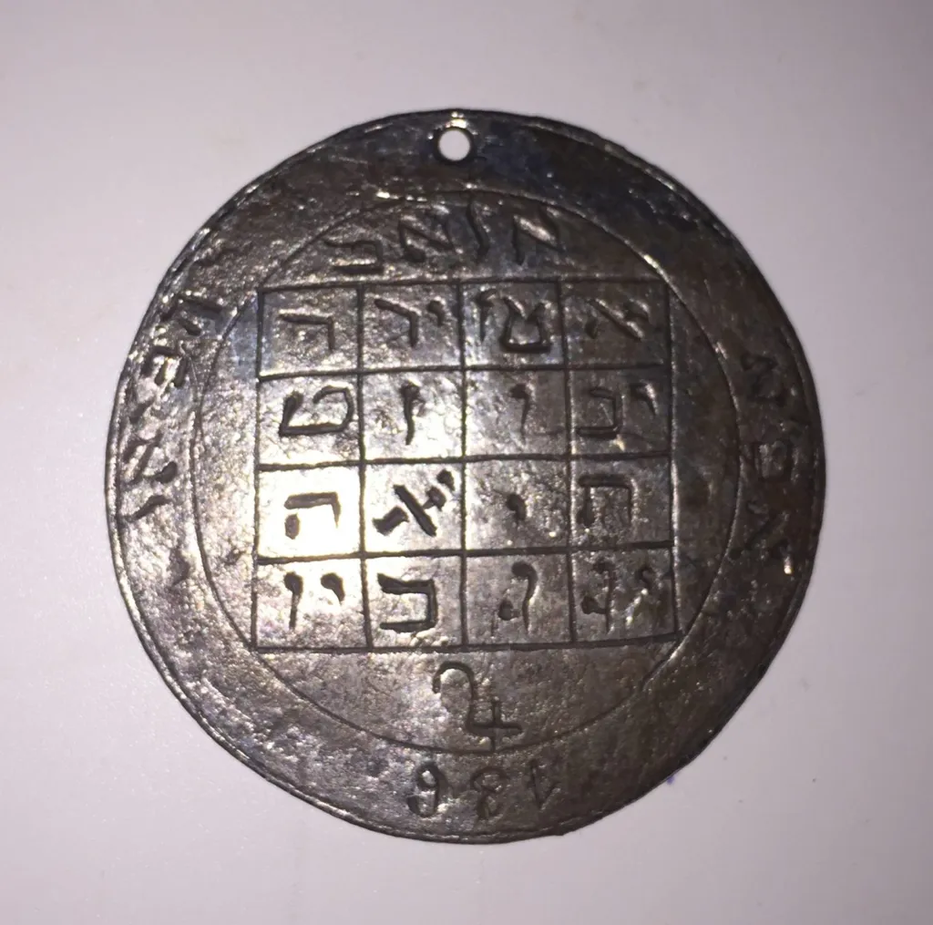Round metal amulet engraved with a four by four grid of Hebrew letters