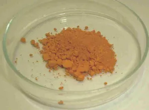 Orange lead chromate pigment powder in a glass dish