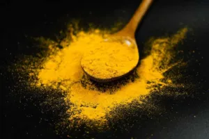 Heaped spoon of bright yellow Curcuma longa powder on a black background