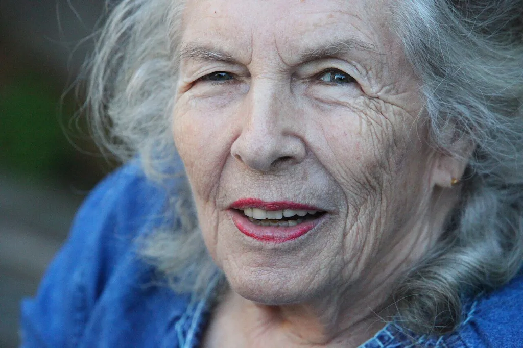 Portrait of Ann Shulgin, white-haired and smiling, in a blue top, 2011