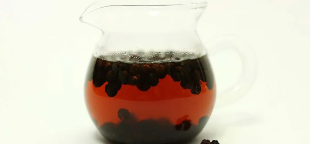 Schisandra chinensis berry tea, dark red liquid with whole berries in a glass jug