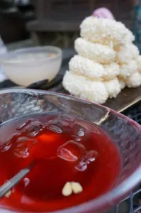 Glass bowl of red Schisandra chinensis omija tea beside white puffed rice sweets