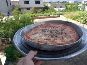 Home-baked pizza in a round pan with black Nigella sativa seeds scattered over the top