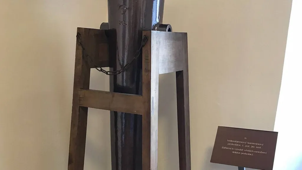 A tall, dark stoneware percolator standing in a wooden frame in a museum of old pharmacy