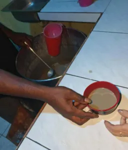 Hands passing a small cup of Piper methysticum kava drink across a table at night in Vanuatu