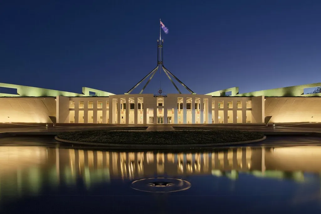 Parliament House, Canberra, lit up at dusk with the flagpole above it